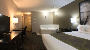 A hotel room with a bed, a desk with a TV, a chair, a bathtub, and a nightstand with a lamp. - Super 8 by Wyndham Kapuskasing (Kapuskasing)