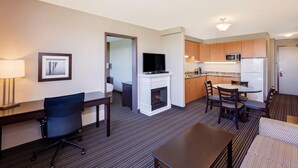 A hotel room with a dining area, a TV, a fireplace, and a kitchenette. - Super 8 by Wyndham Kapuskasing (Kapuskasing)