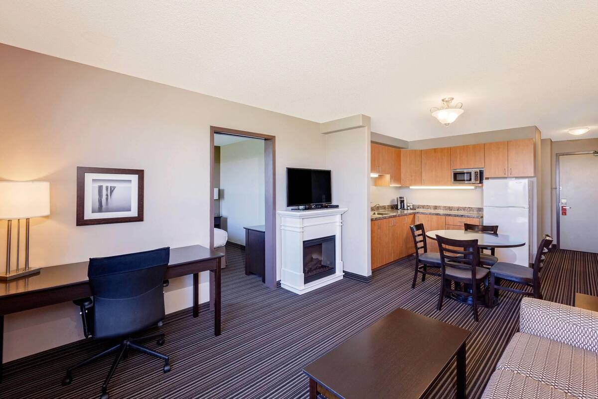 Quarto de hotel com área de jantar, TV, lareira e cozinha compacta.