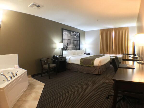 Habitación de hotel con cama, escritorio, silla, lámpara de escritorio, lámpara, televisor, ventana con cortinas y baño con bañera y lavamanos.