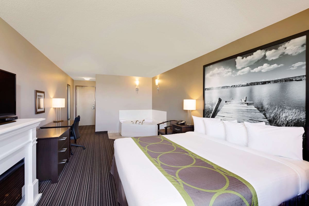 Quarto de hotel com uma cama grande, uma mesa com cadeira, um sofá, uma banheira e uma televisão.
