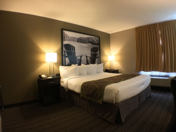 Habitación de hotel con una cama grande, dos mesitas de noche con lámparas, un cuadro enmarcado en la pared y una ventana con cortinas.