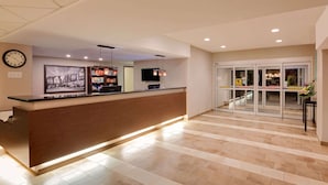 A hotel reception area with a reception desk, a clock, a television, and a glass door entrance. - Super 8 by Wyndham Kapuskasing (Kapuskasing)