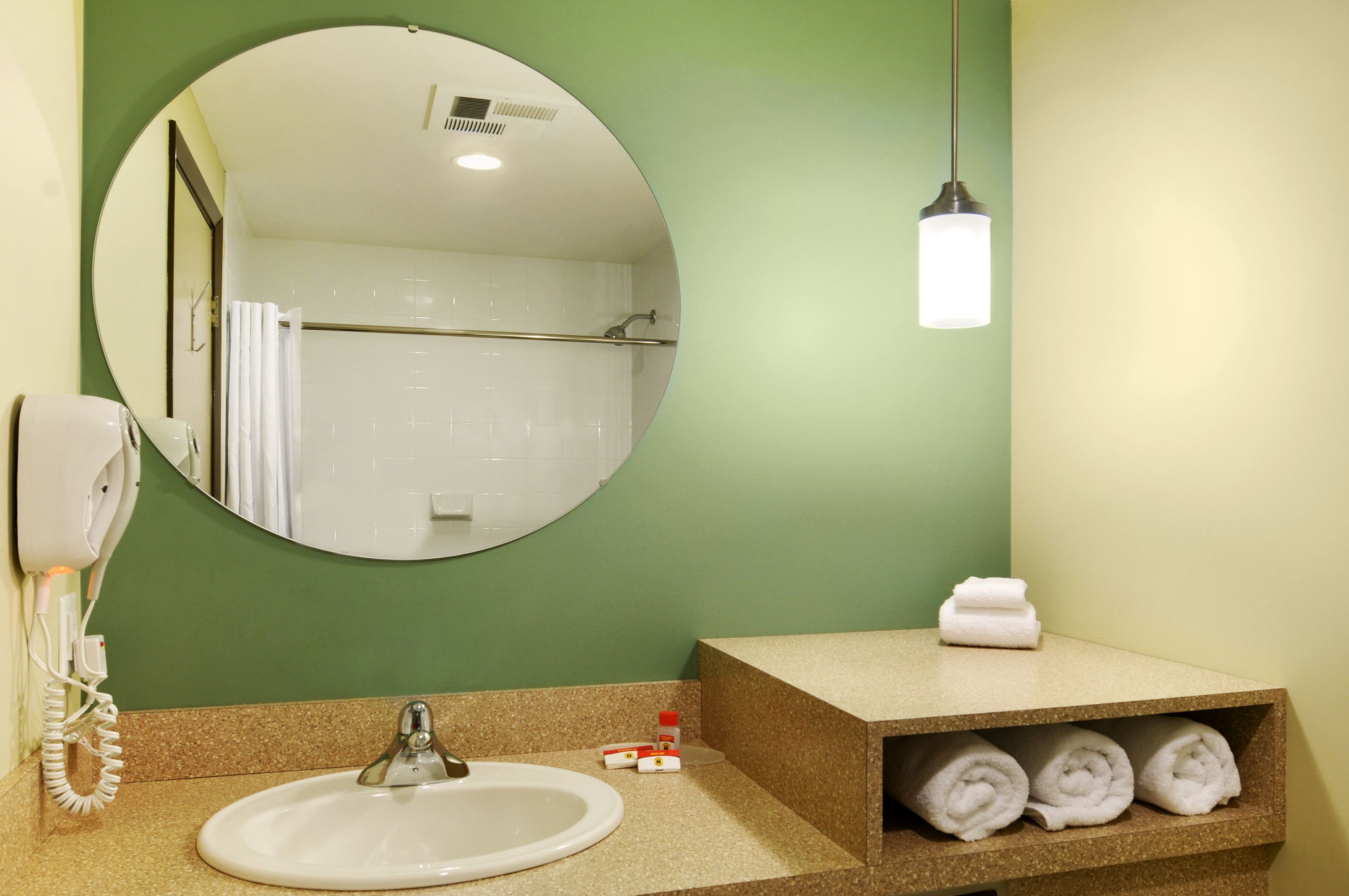 A bathroom with a round mirror, a sink, a towel rack, and a shelf with towels.