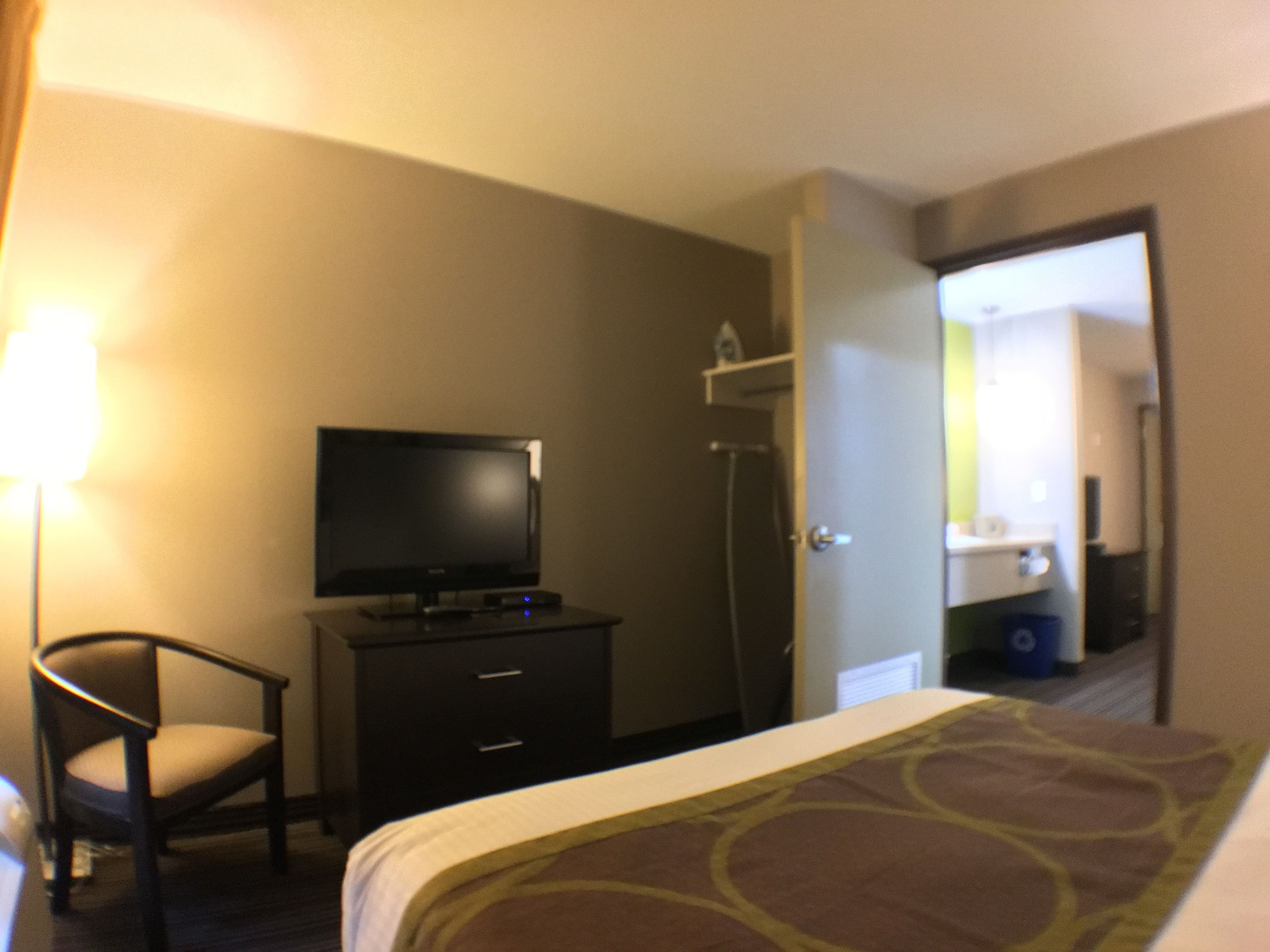 Habitación de hotel con cama, televisor en una cómoda, una silla y baño visible a través de una puerta abierta.