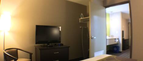 A hotel room with a bed, a television on a dresser, a chair, and a bathroom visible through an open door.