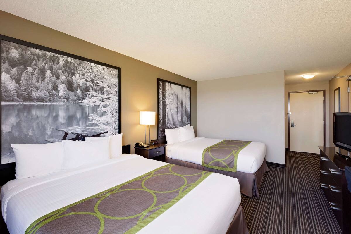 Quarto de hotel com duas camas, uma escrivaninha, uma cadeira, televisão e obras de arte nas paredes.