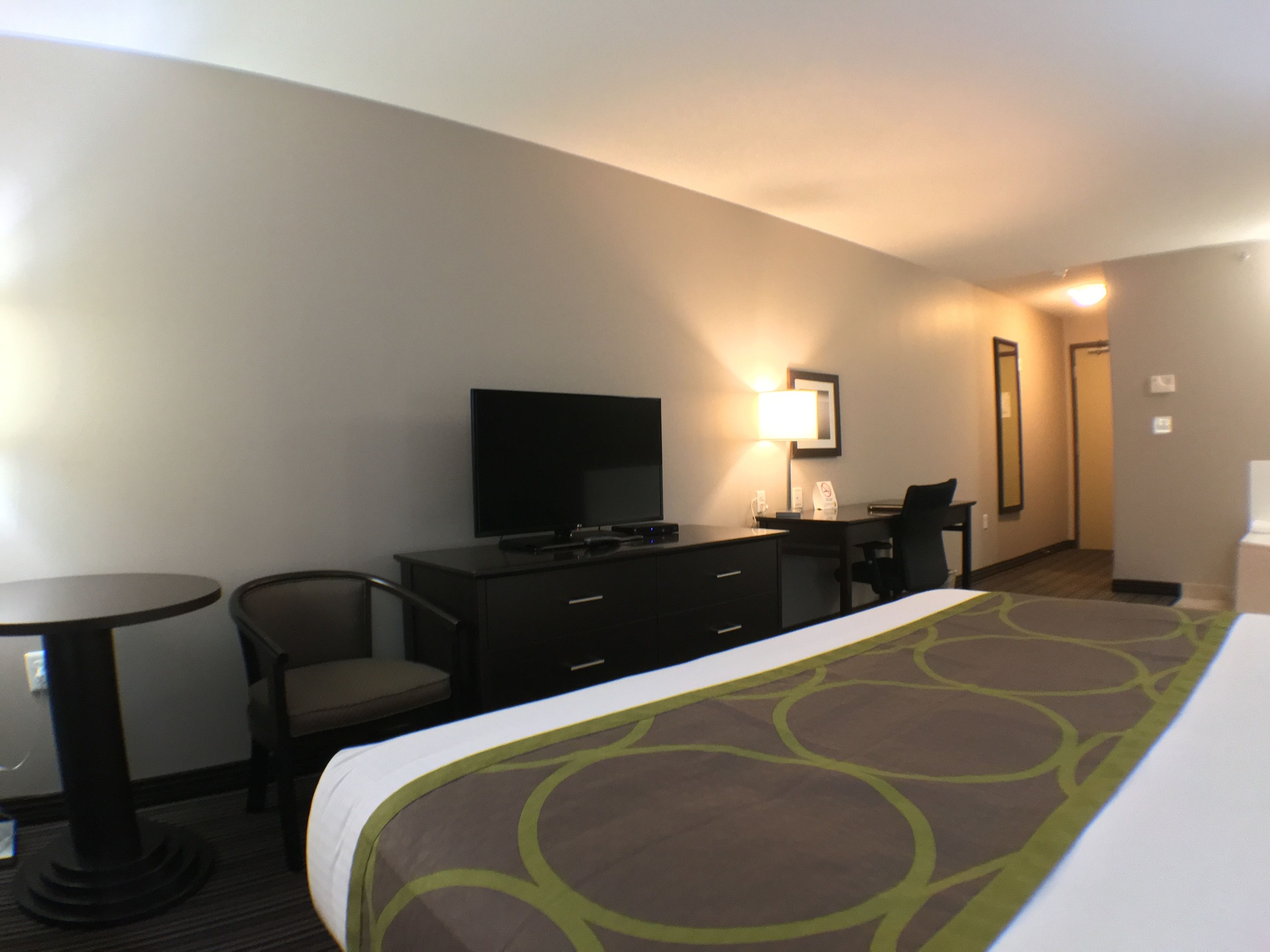 A hotel room with a bed, a desk, a chair, a television, and a lamp.