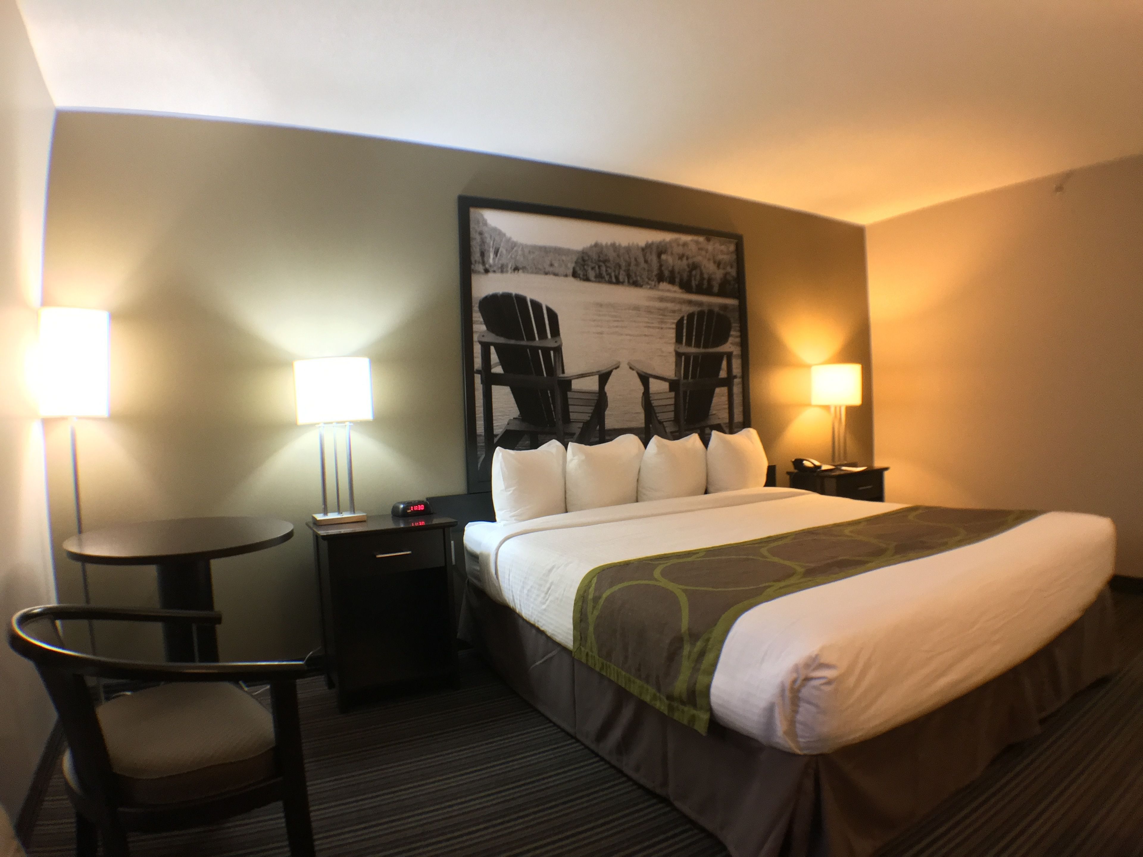 A hotel room with a bed, two chairs, a small table, two bedside lamps, and a framed picture on the wall.