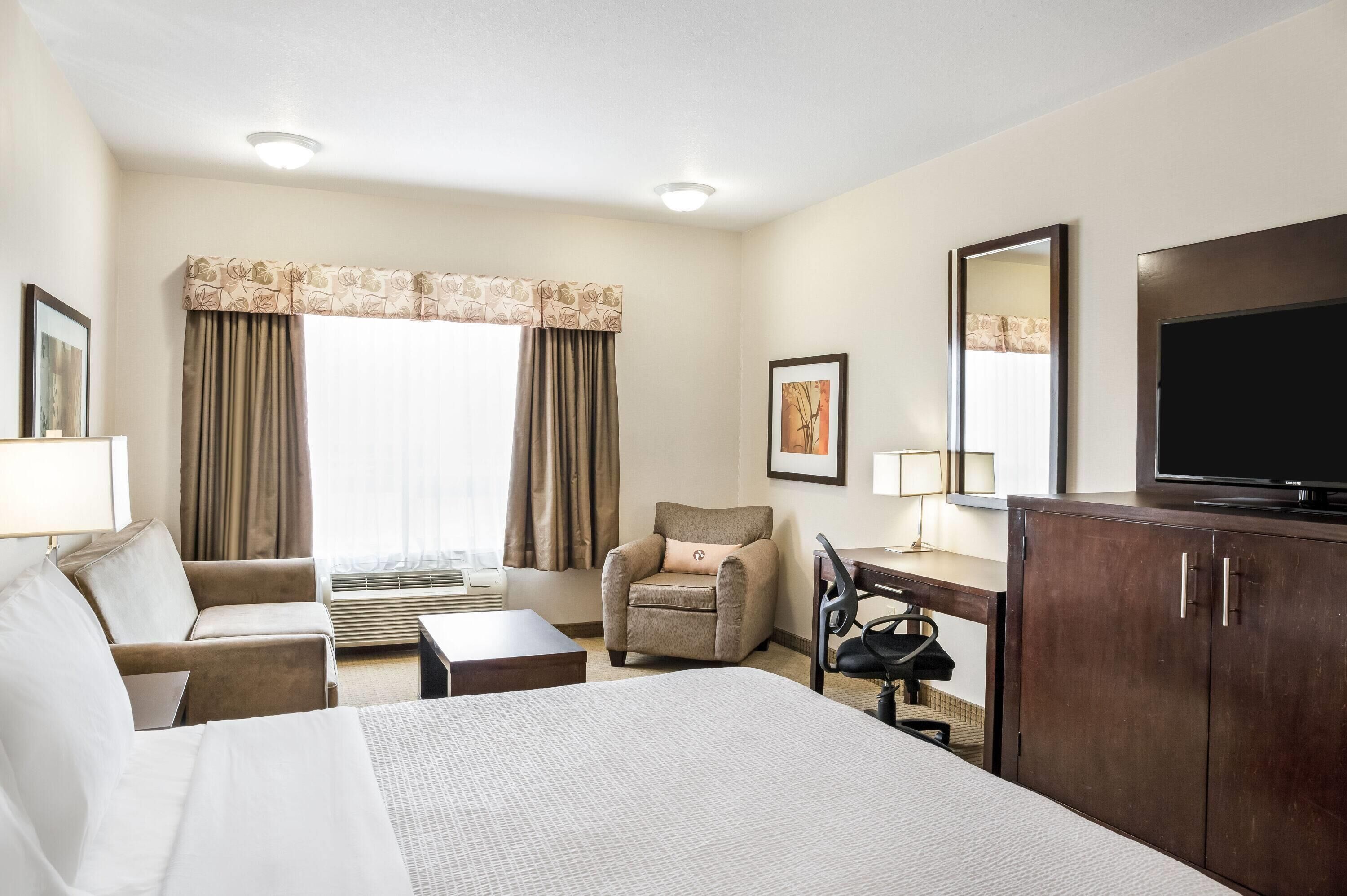 A hotel room with a bed, a desk, a chair, a TV, and a window with curtains.