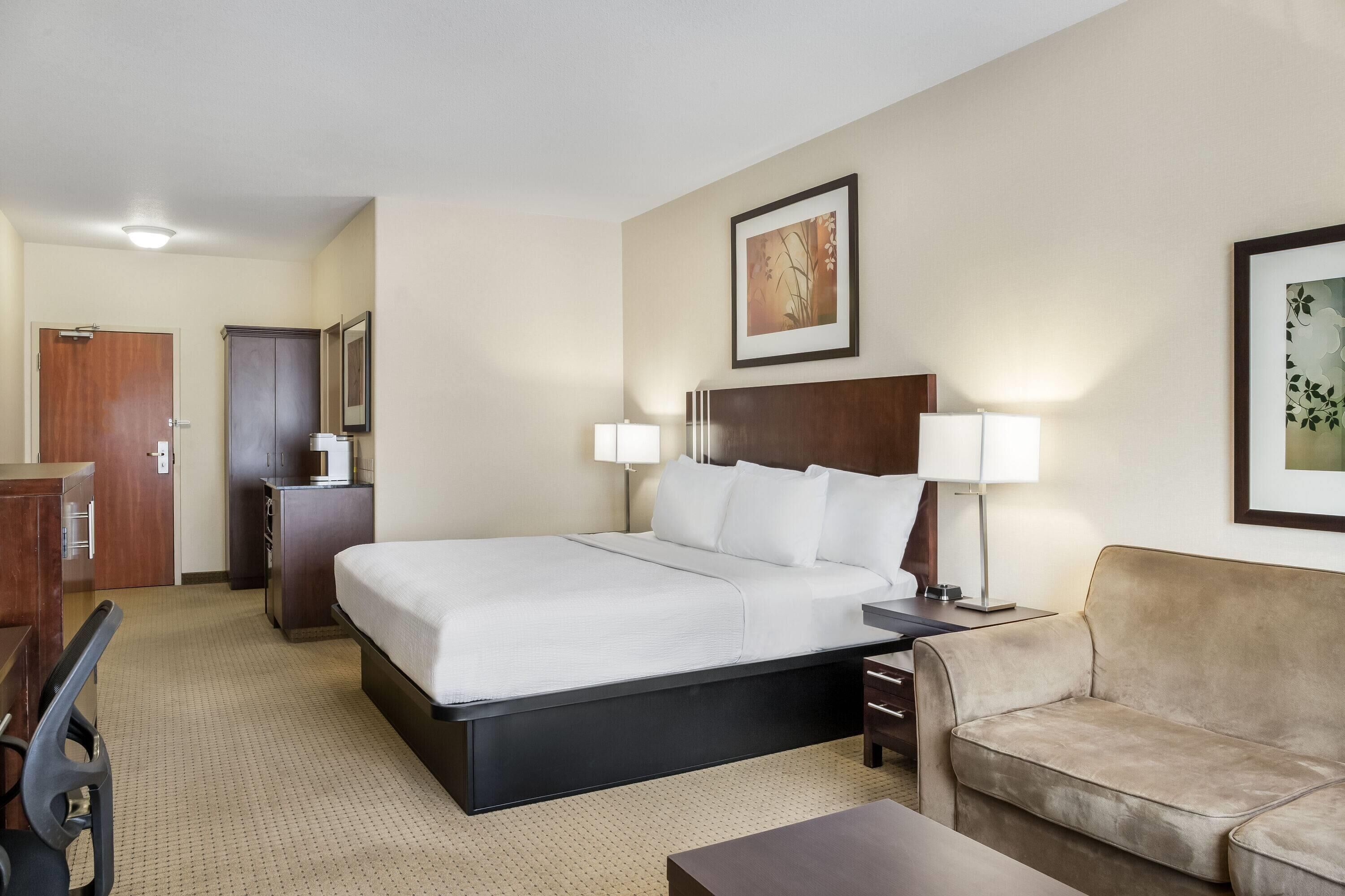 A hotel room with a bed, a desk, a chair, a sofa, and two lamps.