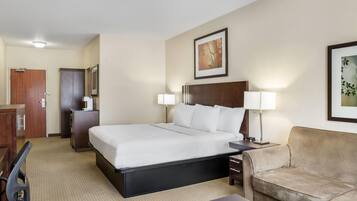 A hotel room with a bed, a desk, a chair, a sofa, and two lamps.