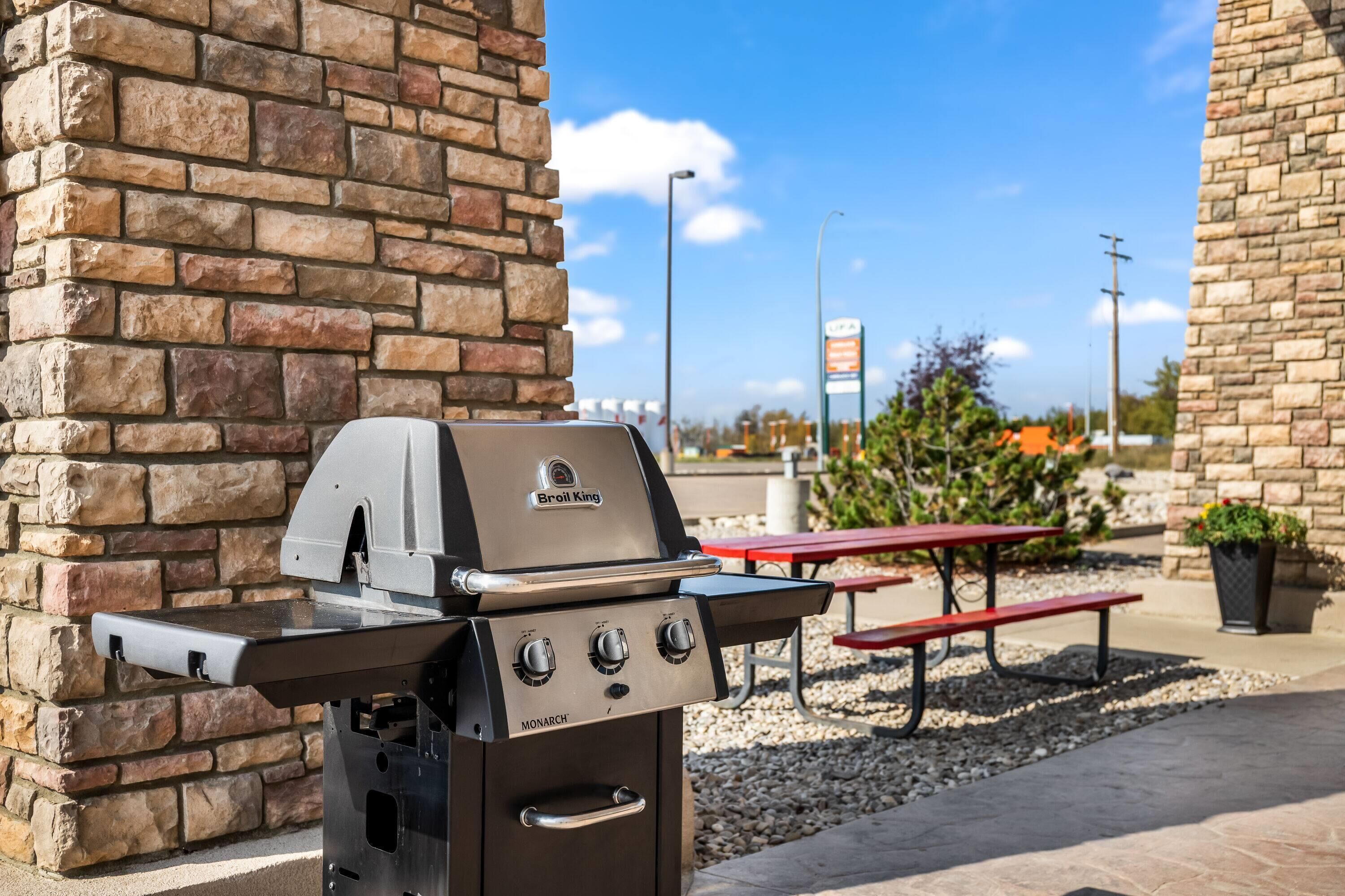 En gasgrill med digitalt display og flere betjeningsknapper, placeret udendørs op ad en stenvæg.
