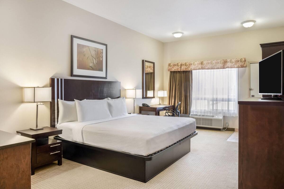 Une chambre d’hôtel avec un grand lit, des tables de chevet, un bureau, une chaise, une télévision et une fenêtre avec des rideaux.