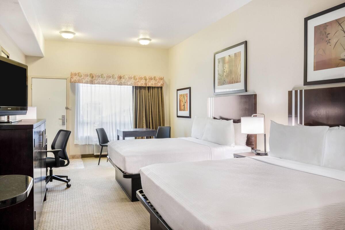 Une chambre d’hôtel avec deux lits, un bureau, une chaise, une télévision et une fenêtre avec des rideaux.