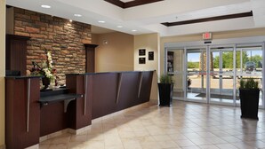 Zona de recepción con pared de piedra, mostrador de recepción y puerta de cristal que da al exterior.