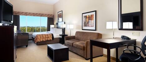 A hotel room with a bed, a sofa, a desk with a chair, a TV, and a large window offering a view.