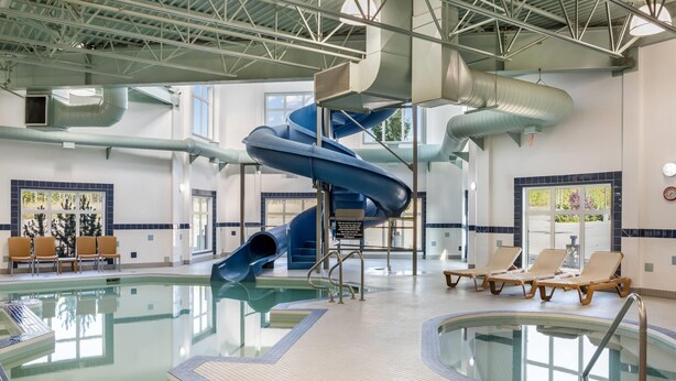 Una piscina interior con tobogán azul, sillas de descanso y suelo de baldosas.