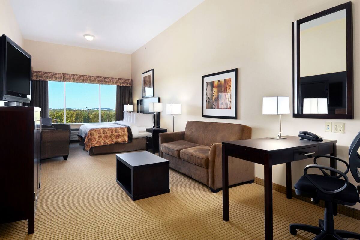 Une chambre d’hôtel équipée d’un lit, d’un canapé, d’un bureau, d’une télévision et d’une grande fenêtre donnant sur un beau paysage.