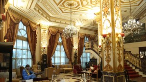 Un vestíbulo imponente con columnas decorativas, una araña central y una escalera.