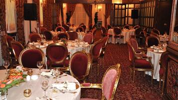 A formal dining room with round tables, red velvet chairs, and gold accents.