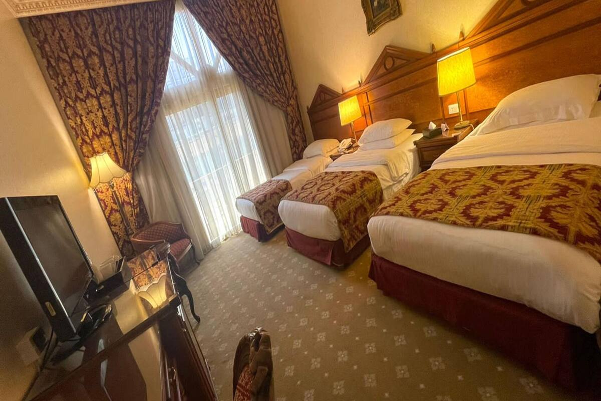 A hotel room with two beds, a desk with a television, and a large window with curtains.