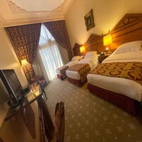 Ein Hotelzimmer mit zwei Betten, einem Schreibtisch mit Fernseher und einem großen Fenster mit Vorhängen.
