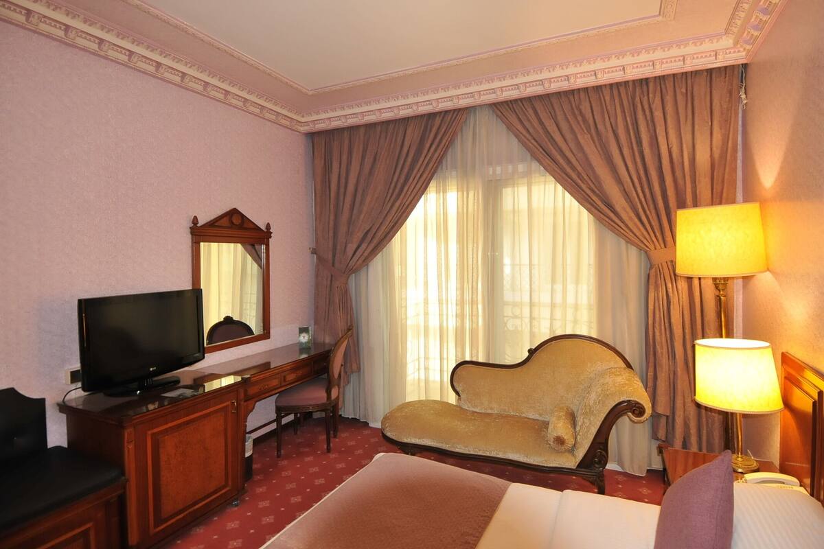 A hotel room with a bed, a desk with a television, a chair, and a lamp.