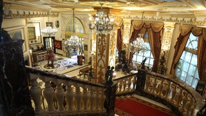 Un lobby de hotel amplio y lujoso, con una escalera de mármol, candelabros y una zona alfombrada en rojo.