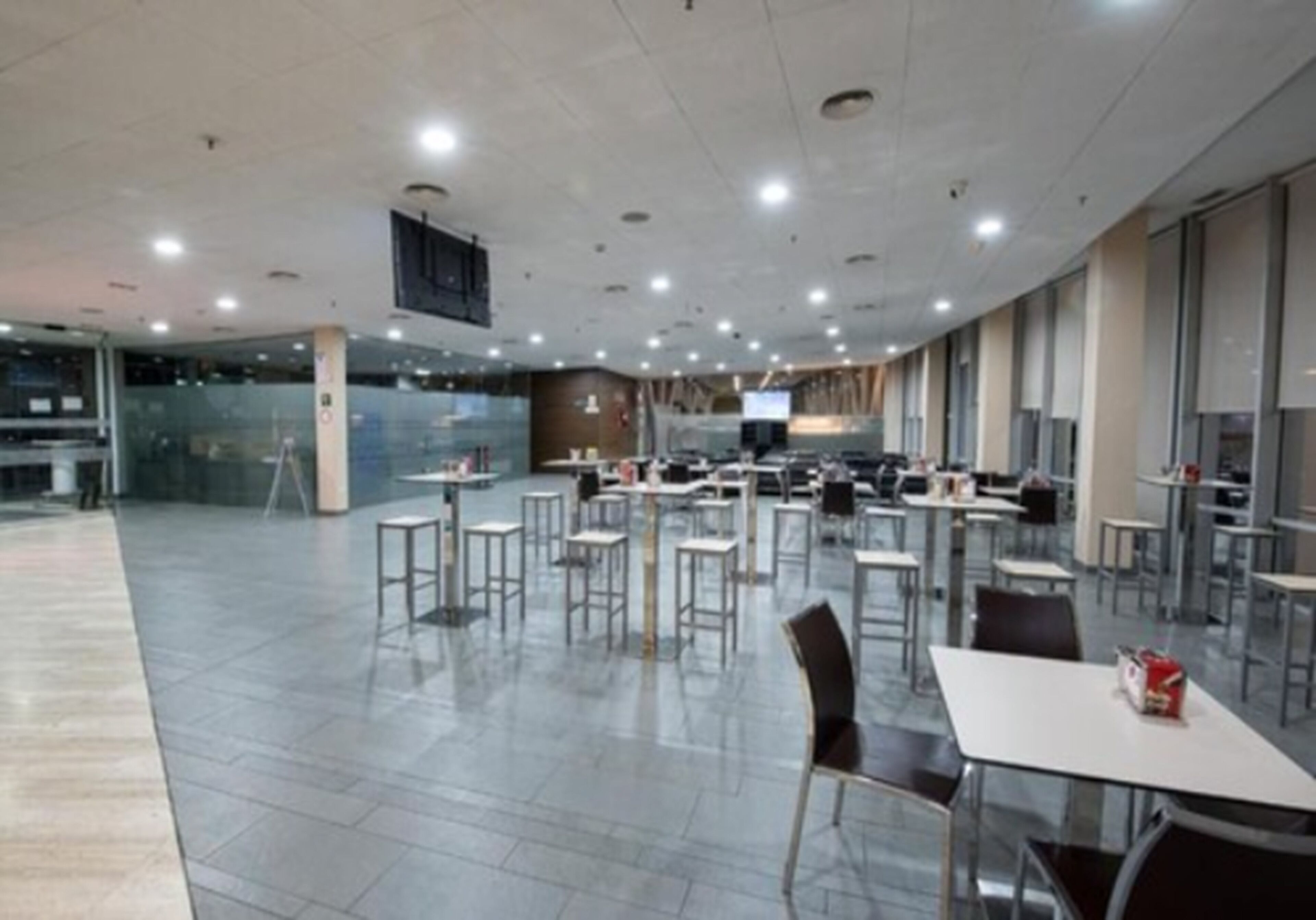 Un espacio interior amplio con varias mesas y sillas, piso llano y techo alto con iluminación empotrada.