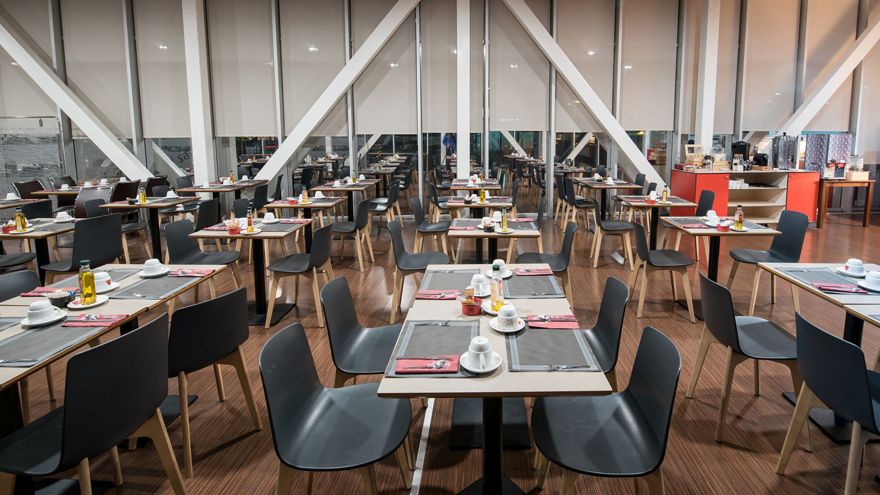 Un'ampia sala da pranzo con diversi tavoli e sedie, ampie finestre e un design d'interni moderno.
