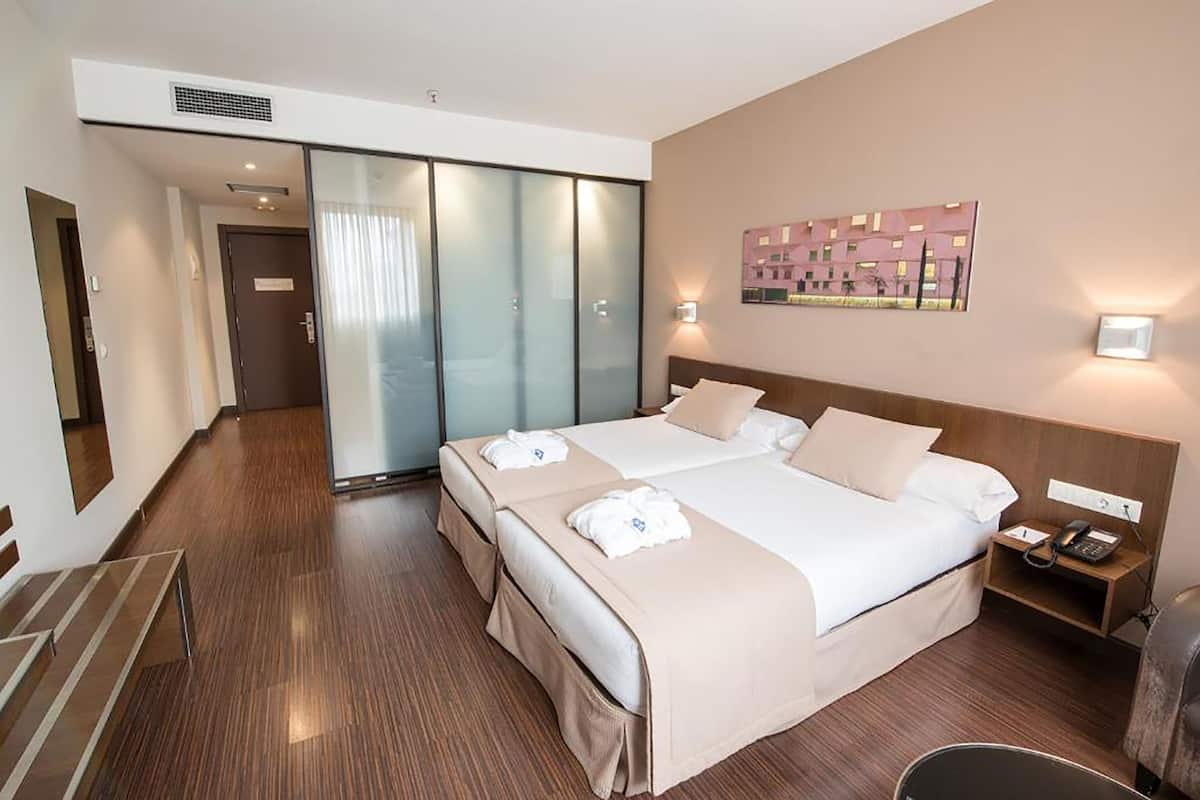 Hotellihuone, jossa on suuri sänky, yöpöytä, jossa on puhelin, ja seinälle kiinnitetty taideteos.