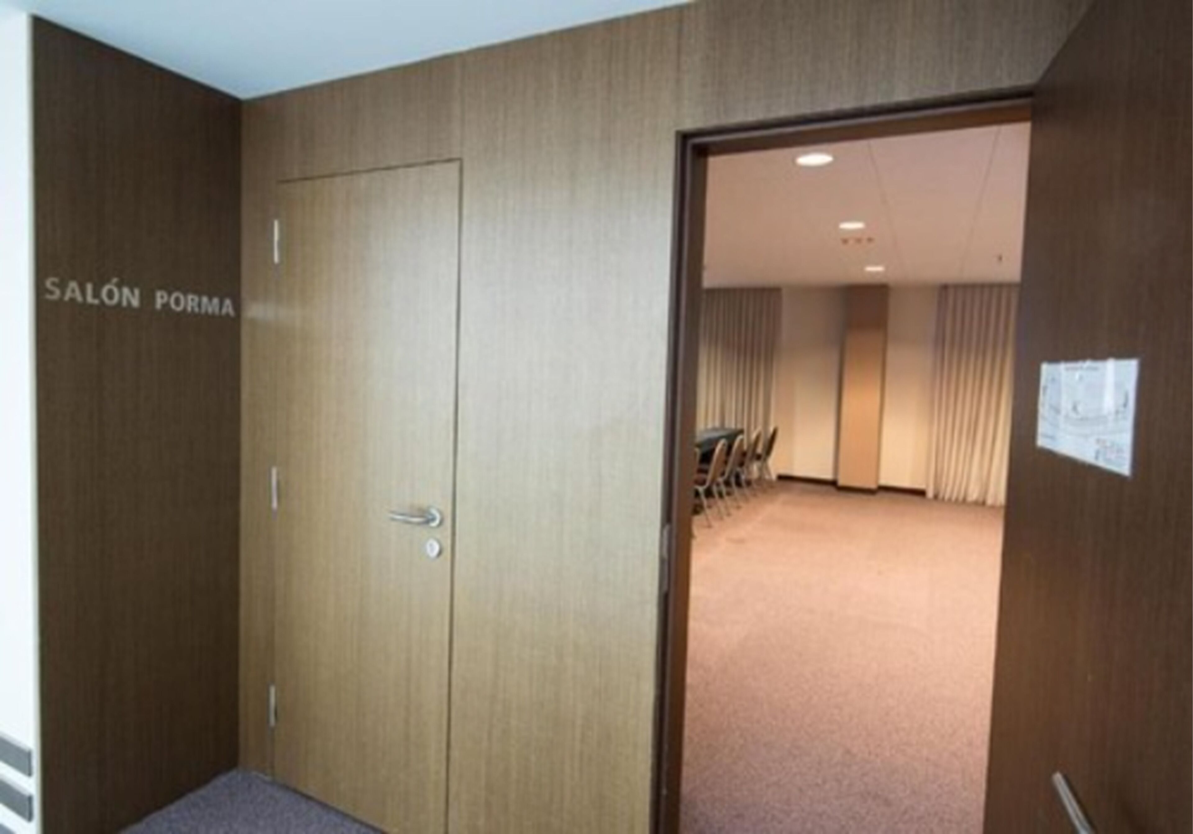 A hotel room with a closed door labeled "SALÓN PORMA" and a view into a conference room with chairs and a carpeted floor.