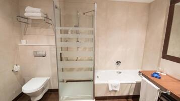 Un baño moderno con ducha envuelta en vidrio, inodoro blanco, bañera y tocador de madera con perchero.