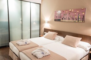A hotel room with two beds, a large window, a painting on the wall, and a robe on the bed. - Hotel Abad San Antonio (León)