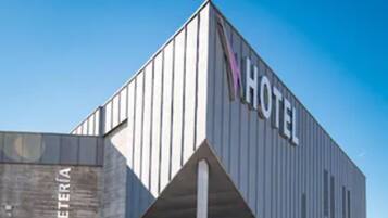 Un hotel moderno con un llamativo letrero 'HOTEL', fachada de hormigón y una entrada pavimentada con bolardos.