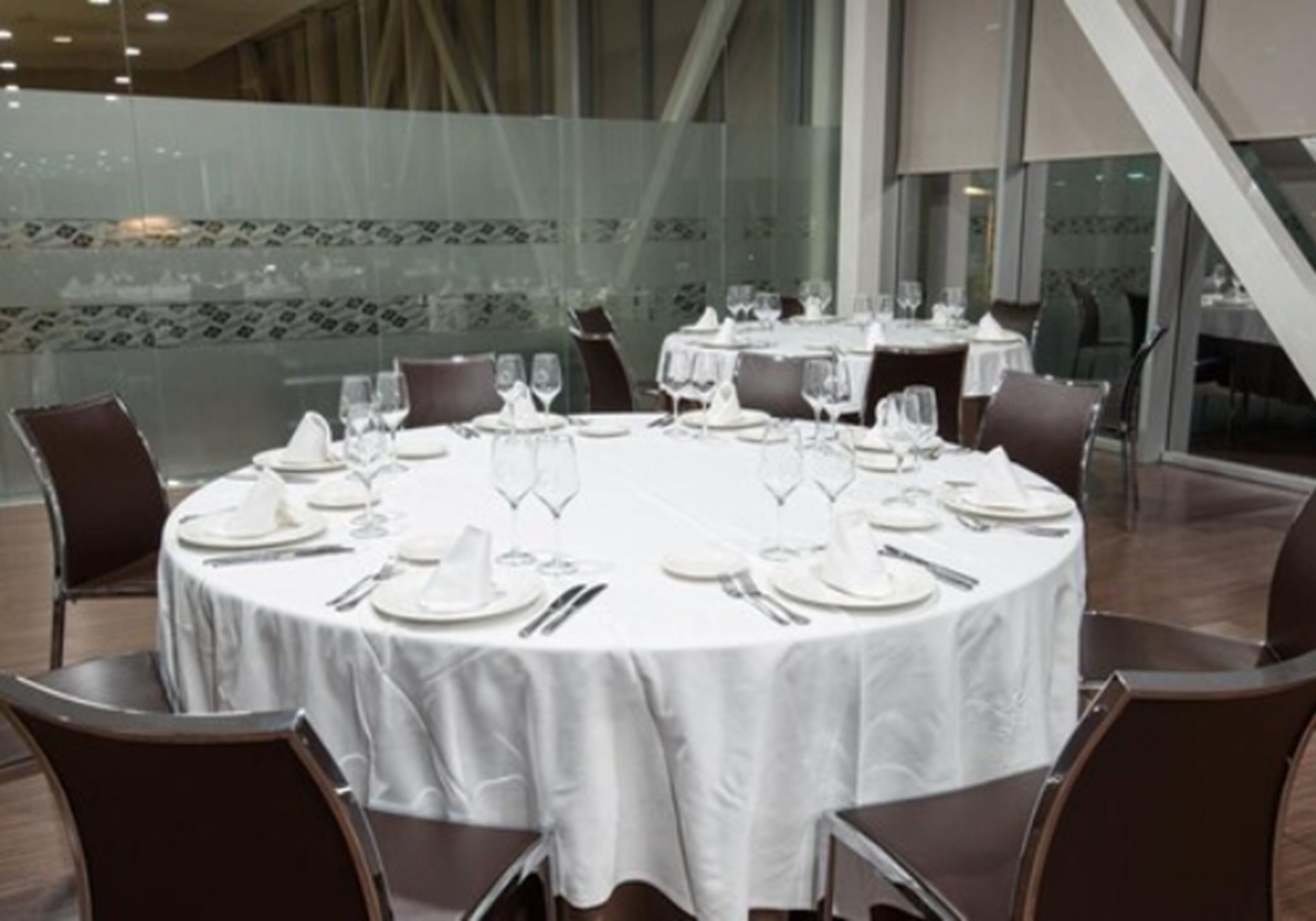 A round dining table set for four with white tablecloths, surrounded by dark chairs.