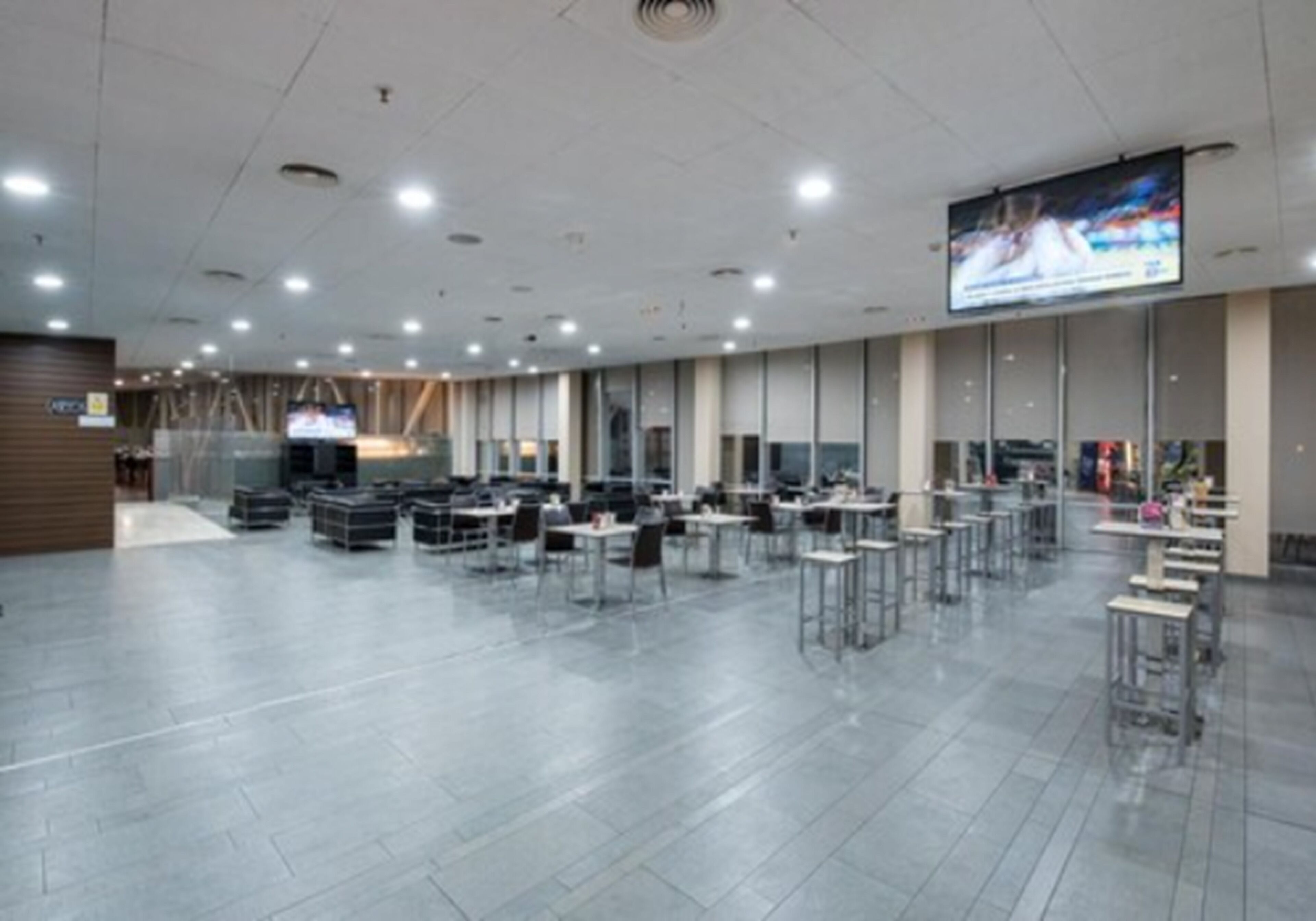 A spacious indoor area with multiple tables and chairs, a large screen displaying an image, and a modern architectural design.