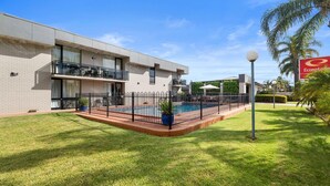 Un edificio moderno con piscina, rodeado por una cerca y un césped bien cuidado.