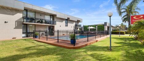 Um edifício moderno com piscina, cercado por uma vedação e um gramado bem cuidado.