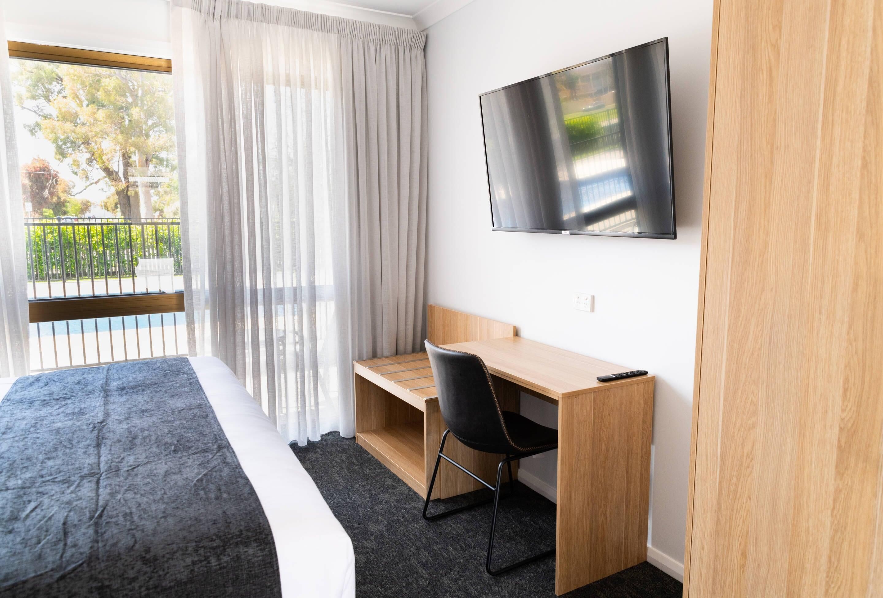 Habitación de hotel con cama, escritorio, silla, televisión y ventana con cortinas.
