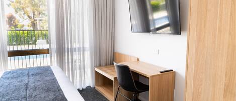 Habitación de hotel con cama, escritorio, silla, televisión y ventana con cortinas.
