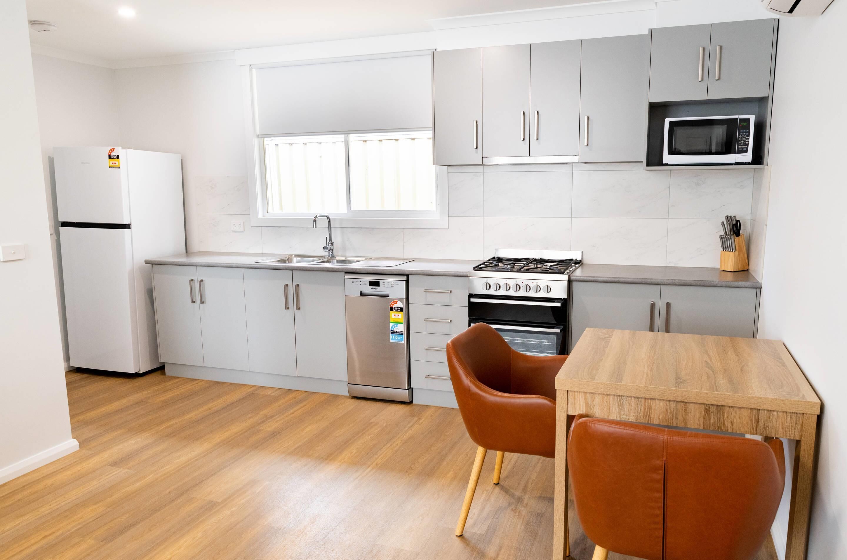 Una cocina moderna con armarios blancos, un refrigerador de acero inoxidable, un horno empotrado y un microondas.