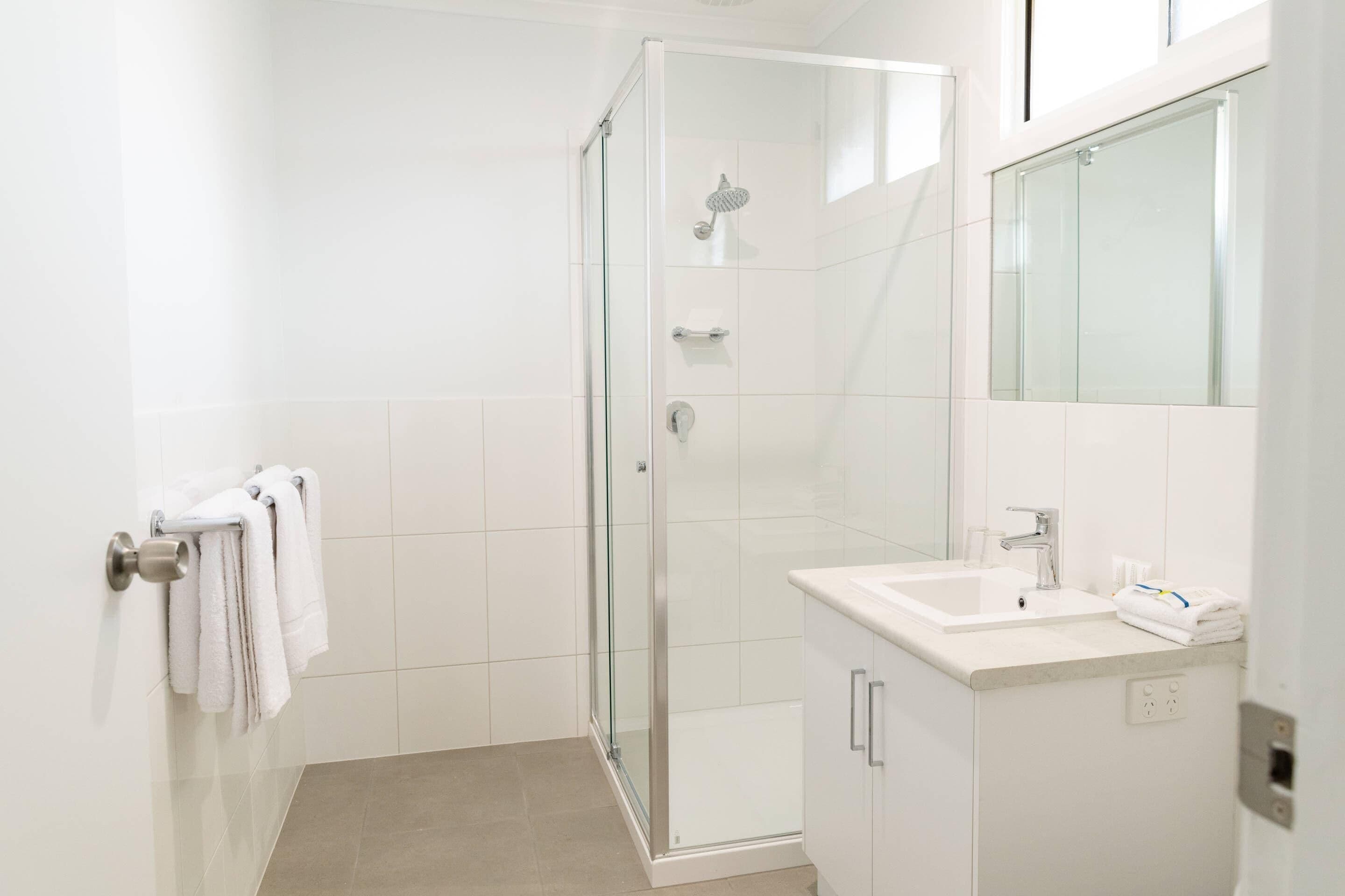 A modern bathroom with a glass-enclosed shower, a white sink, and a mirror above it.