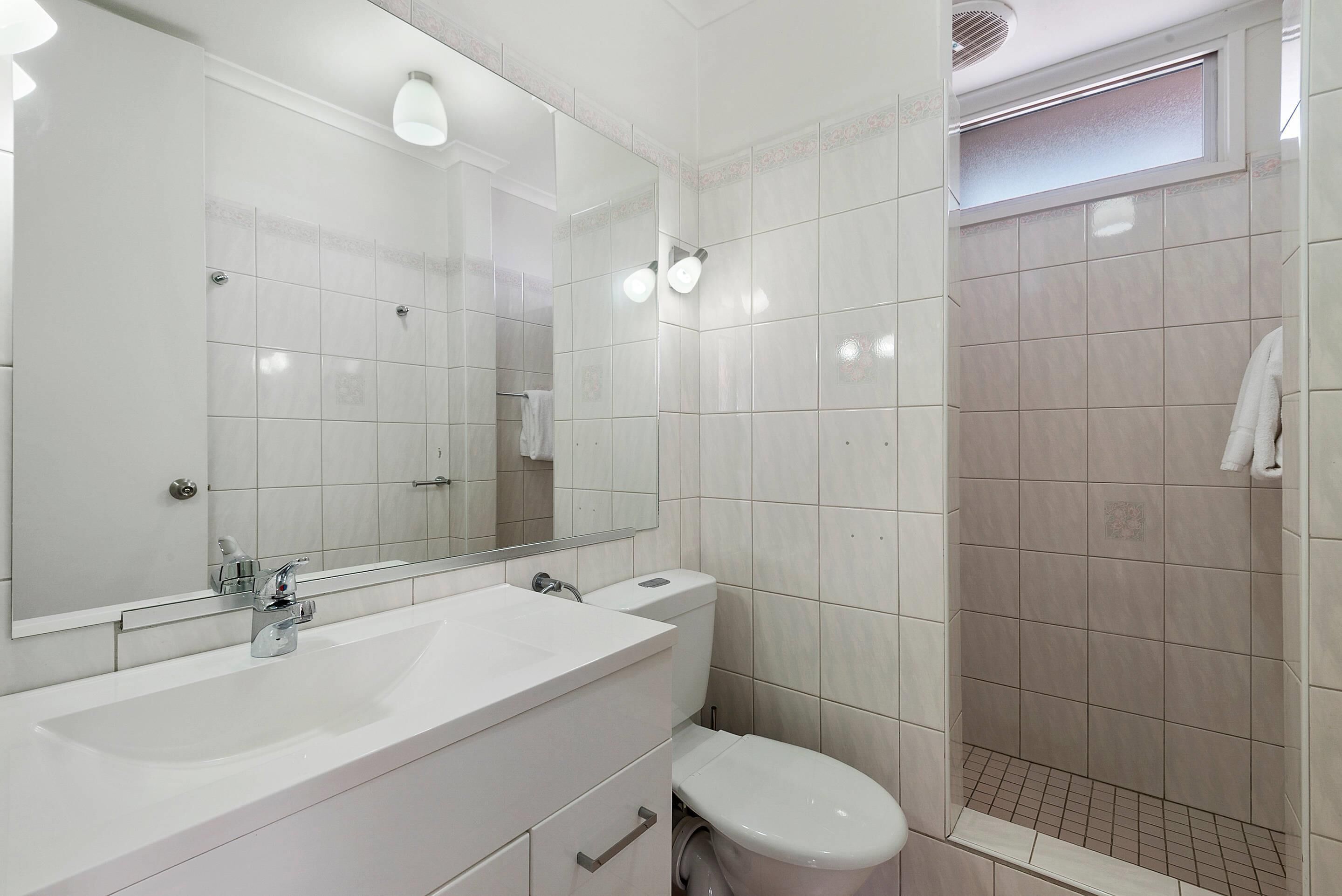 A modern bathroom with a large mirror, white sink, and a shower area.