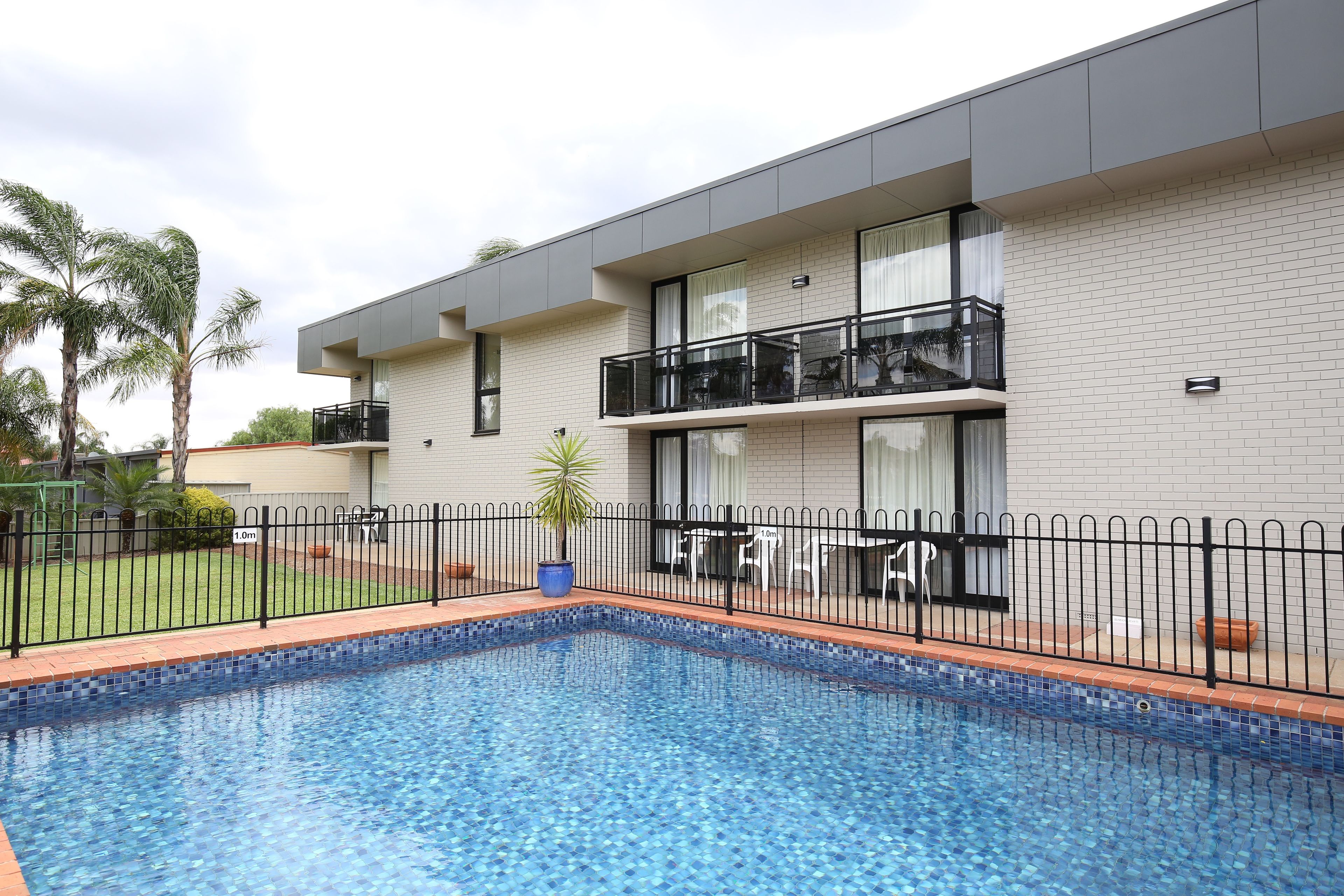 Un edificio moderno con piscina, patio cercado y balcón con mobiliario exterior.