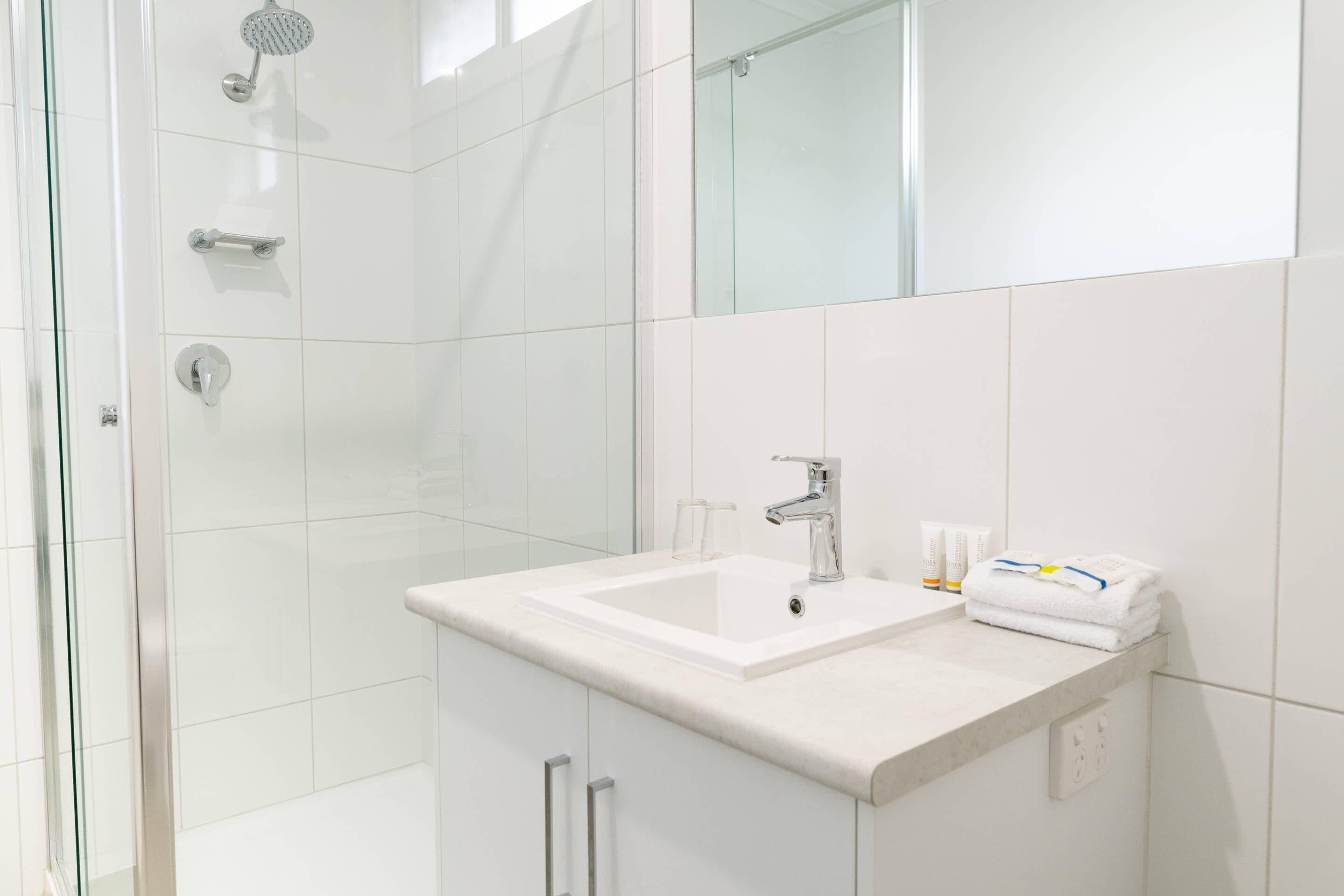 A modern bathroom with a glass shower enclosure, a white sink with a mirror above, and toiletries on the counter.