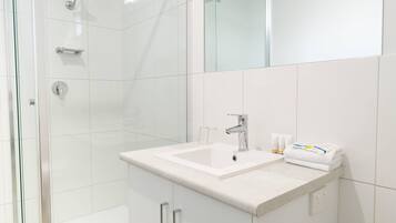 A modern bathroom with a glass shower enclosure, a white sink with a mirror above, and toiletries on the counter.
