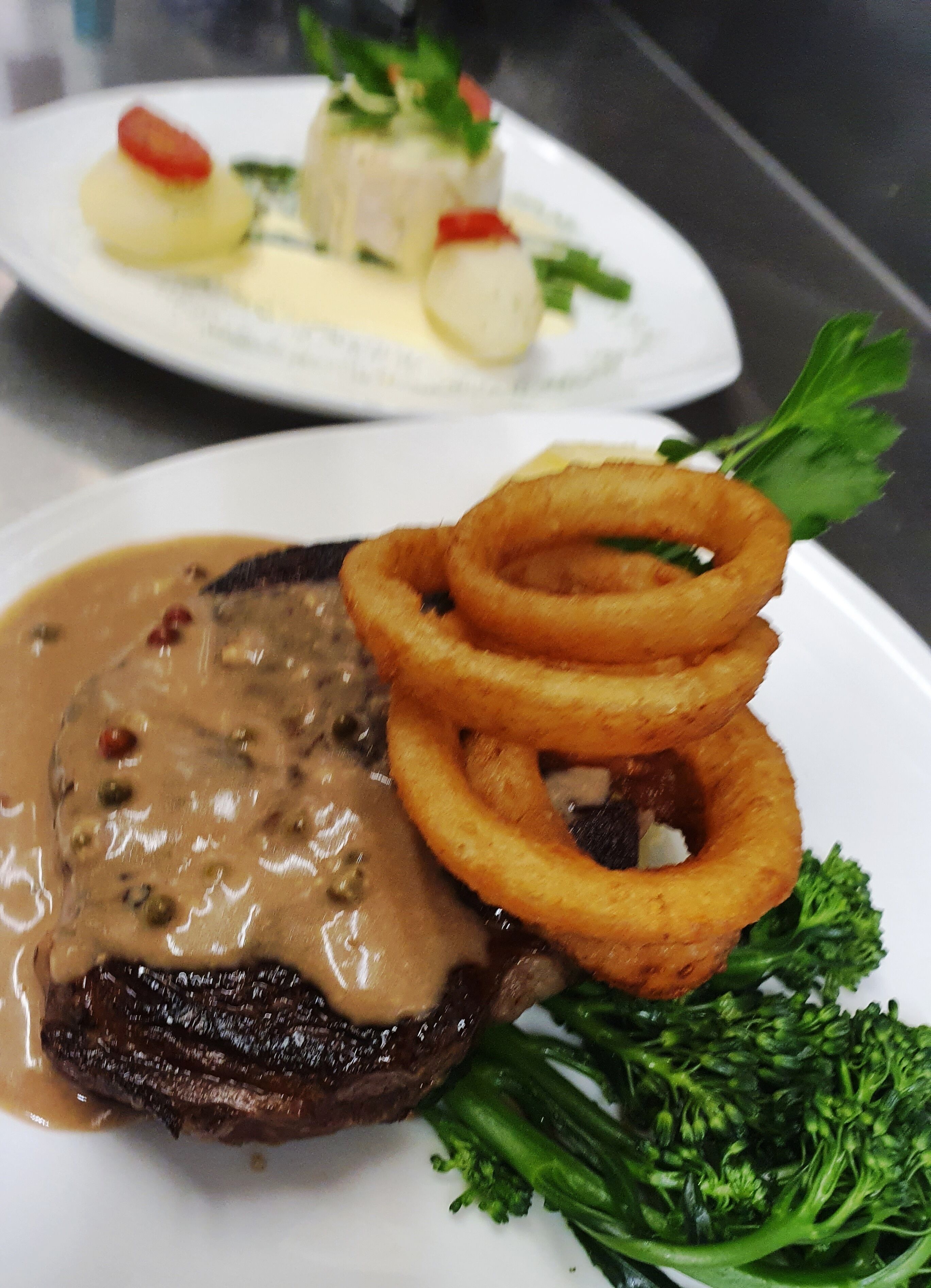 Een bord met steak, overgoten met champignonsaus, uienringen en broccoli.