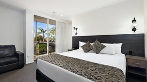 Habitación de hotel con una cama grande, un sofá de cuero negro, un balcón con vistas y un diseño moderno.